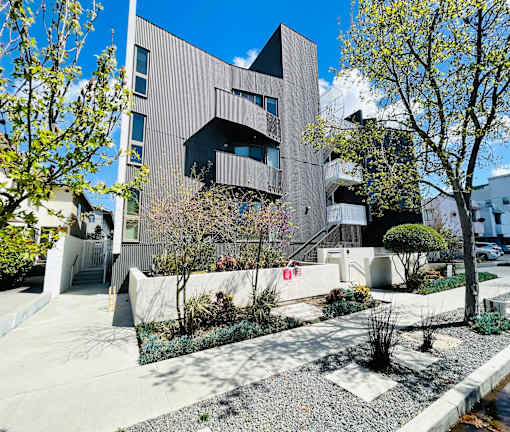 A modern building with a grey facade and a landscaped garden in front.