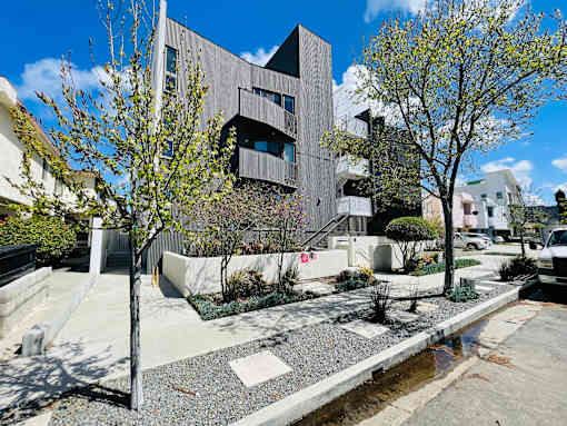 A modern building with a grey facade is surrounded by a garden with a small pond.