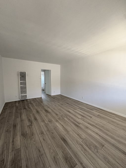 A room with wooden flooring and a doorway leading to another room.