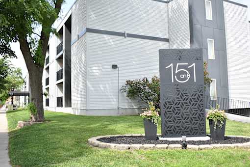 A grey sign with the number 151 on it in front of a building.