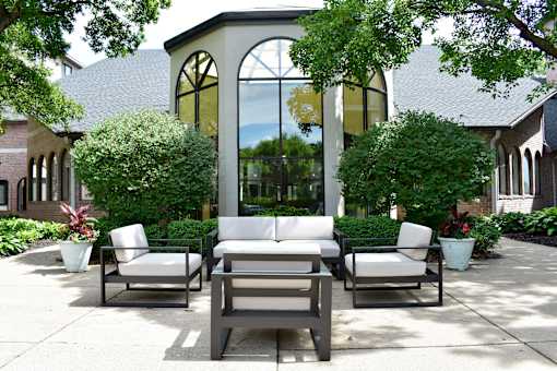 A patio with a couch, chairs and plants.