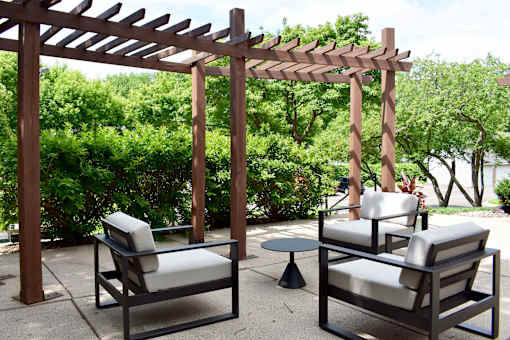 Two chairs and a table are under a wooden pergola.