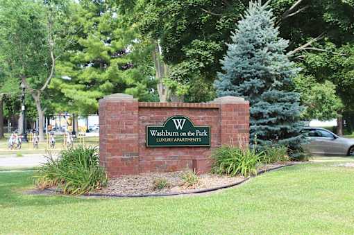 A sign for Washburn on the Park Luxury Apartments is displayed in front of a tree.