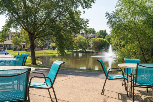 Outdoor patio with blue chairs, round tables, and a view of a lake with a fountain