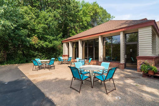 Outdoor patio with blue chairs and round tables in front of the indoor pool building