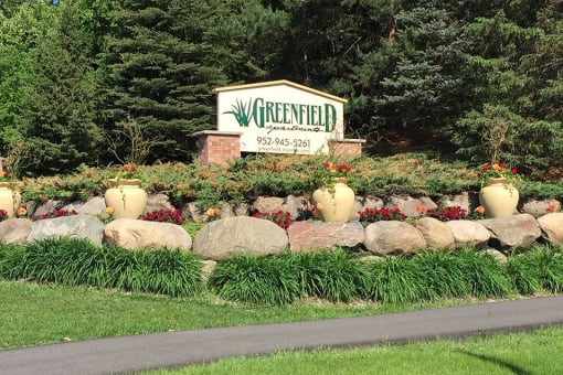 Outdoor property sign atop grass and large rocks that reads "Greenfield"