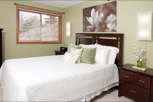 Bedroom with white comforter, decorative pillows, wooden headboard, and artwork of flowers hanging on the wall