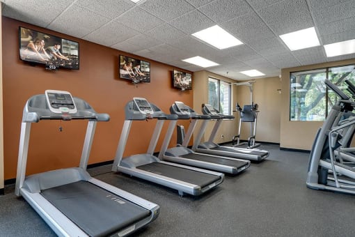 Fitness center with a row of treadmils and TVs on the wall