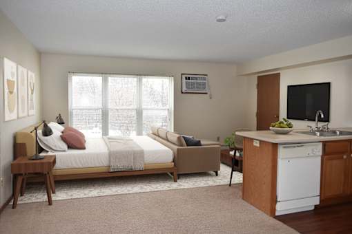 A bedroom with a bed, a couch, a chair, and a kitchenette.
