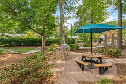 a picnic table with an umbrella and a hammock in a park at Clarion Crossing Apartments, PRG Real Estate Management, Raleigh