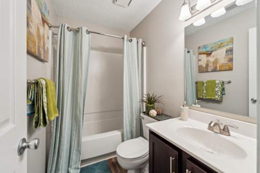 A bathroom with a white toilet, a sink, and a shower with a blue shower curtain. at The Timbers Apartments, Virginia, 23235