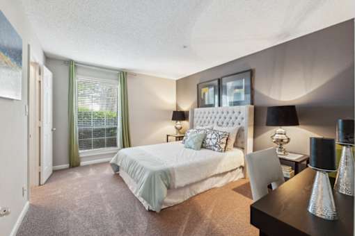A bedroom with a large bed and a desk with a chair. at The Timbers Apartments, Richmond, VA, 23235
