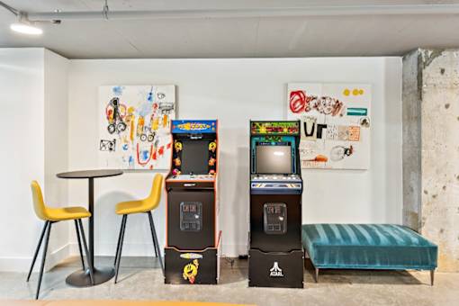 A room with a table, two chairs, a sofa, and two arcade machines at The Box, Richmond, VA, 23224