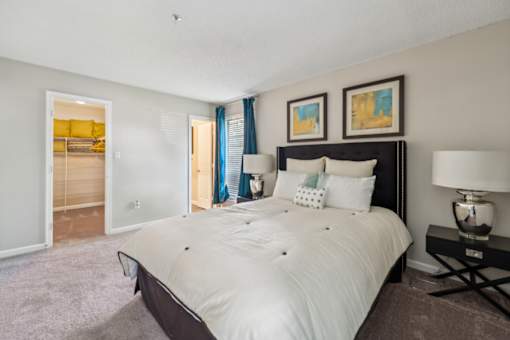 A bedroom with a large bed and a nightstand with a lamp. at The Timbers Apartments, Richmond, Virginia