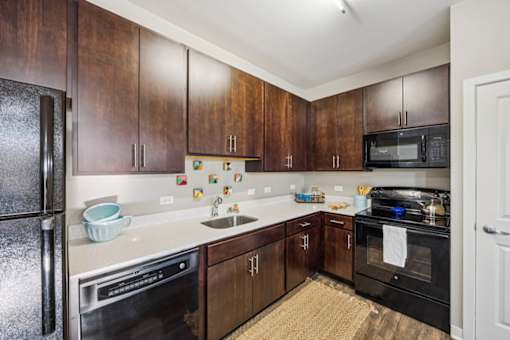 A kitchen with dark wood cabinets and black appliances. at AMP Apartments, Louisville
