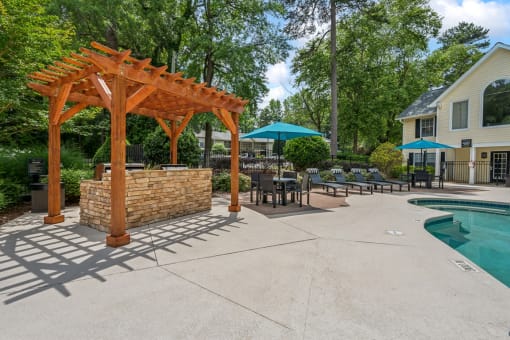 a backyard with a pool and a wooden pavilion with tables and umbrellas at Clarion Crossing Apartments, PRG Real Estate Management, Raleigh