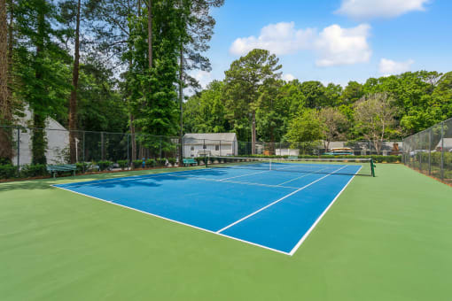 a tennis court with blue and green turf and a fence and trees at Lake Johnson Mews, Raleigh