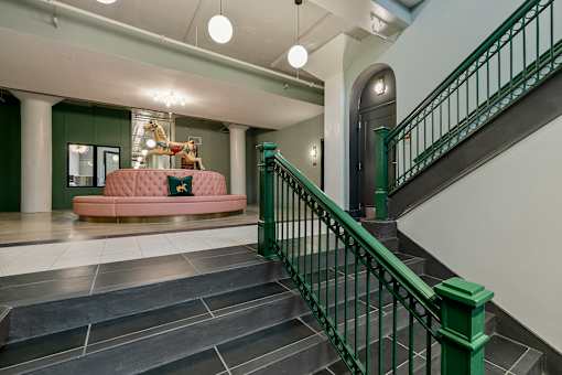 A staircase with a green railing and a pink couch in the background at The Carousel Apartments, Richmond, 23220