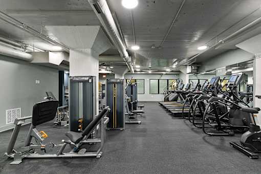 A gym with a variety of equipment including treadmills, stationary bikes, and weight machines at The Carousel Apartments, Richmond