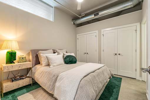 A bedroom with a bed, nightstand, and two green pillows at The Carousel Apartments, Richmond, Virginia