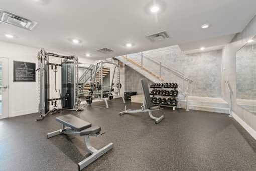 A gym with a variety of equipment including a bench, weights, and a squat rack at South Falls Tower Apartments, Richmond, VA, 23224