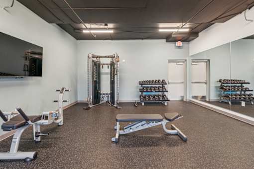 A gym with a variety of equipment including weights and benches  at The Waterford At Rocketts Landing Apartments, PRG Real Estate, Richmond, Virginia