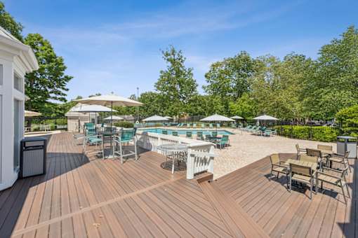 A wooden deck with chairs and umbrellas overlooking a pool. at The Timbers Apartments, Richmond, VA