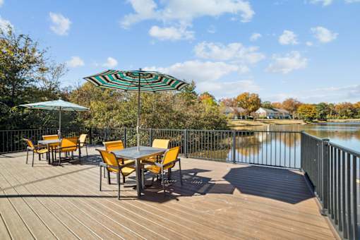 A table with chairs and an umbrella on a wooden deck overlooking a lake at Lakecrest Apartments, PRG Real Estate Management, Greenville, SC, 29615