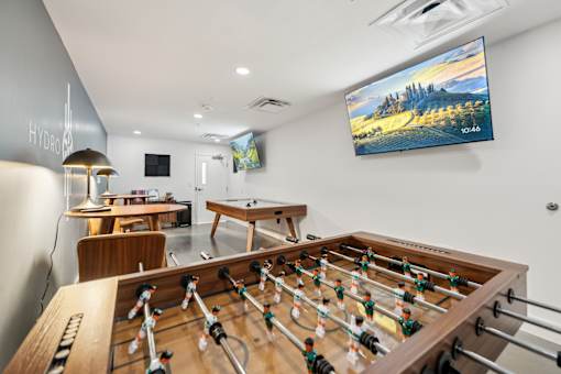 A foosball table is in the middle of a room with a pool table and a ping pong table.