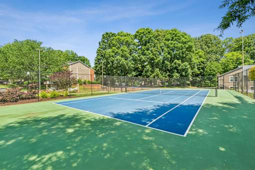 A tennis court surrounded by trees and a fence. at Woodcreek Apartments, North Carolina, 27511