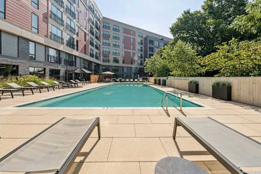 A pool surrounded by sun loungers and a building in the background.