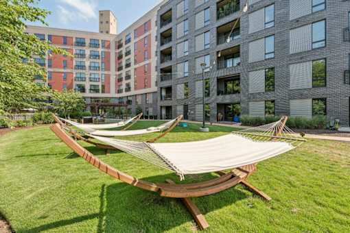 A hammock is set up in a grassy area in front of apartment buildings.