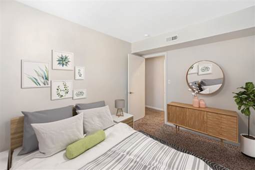A bedroom with a bed, nightstand, and a round mirror on the wall at Rivers Landing Apartments, Hampton, VA