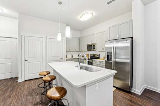 A white kitchen with a refrigerator, sink, and bar stools at Proximity Apartments, South Carolina, 29414