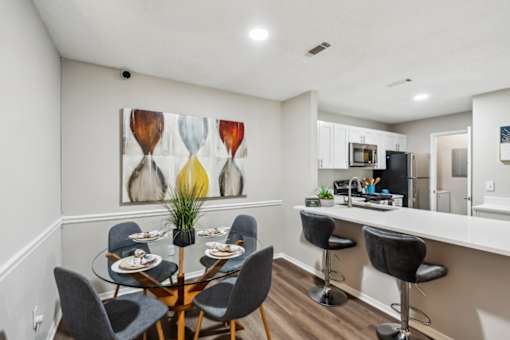A dining room with a table set for six and a painting on the wall.