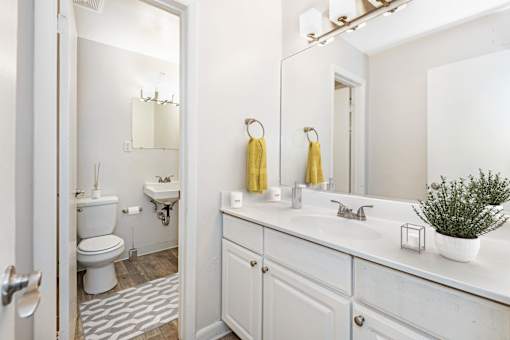 A white bathroom with a toilet, sink, and mirror at Rivers Landing Apartments, Hampton 23666