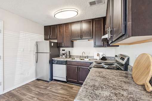A kitchen with wooden cabinets and a granite countertop at The Falls Apartments in Raleigh NC
