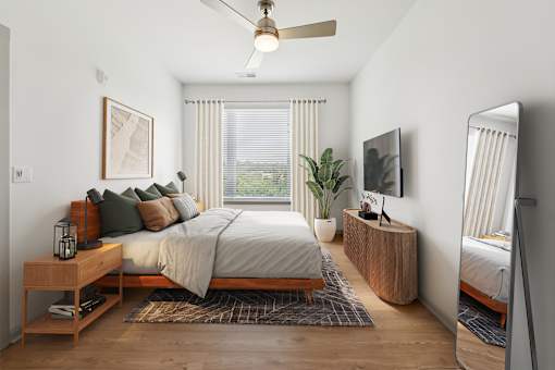 A bedroom with a bed, a nightstand, a plant, and a television  at The Waterford At Rocketts Landing Apartments, PRG Real Estate, Richmond, Virginia