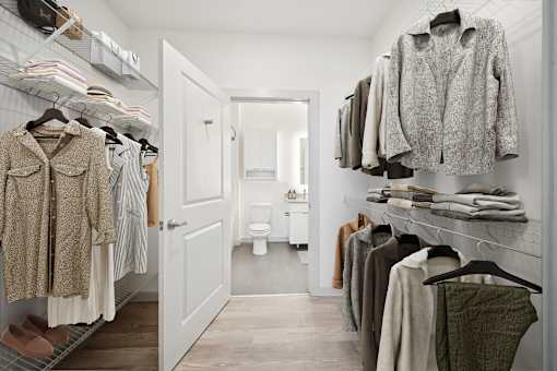 A walk in closet with clothes hanging and a toilet in the background at Circ Apartments, Virginia