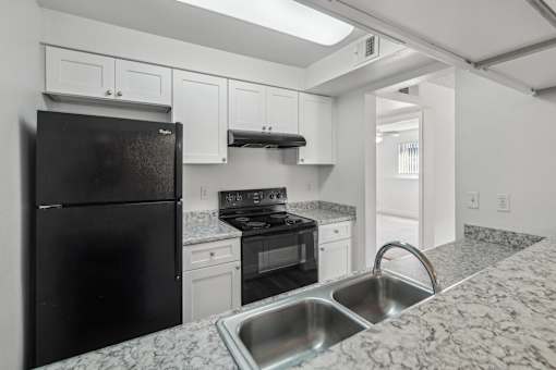 A black refrigerator is in a kitchen with granite countertops.