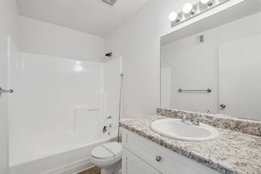 A white bathroom with a marble countertop and a toilet.