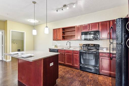 A kitchen with red cabinets and black appliances at Overlook at Stone Oak Park Apartments, San Antonio