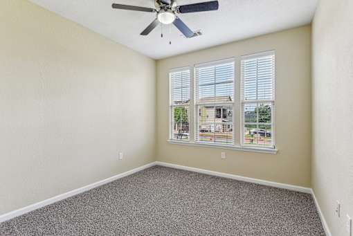 A room with a ceiling fan and a window showing a view of a house at Overlook at Stone Oak Park Apartments, San Antonio