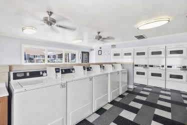 A laundry room with a checkered floor and a row of washers and dryers at North Mountain Apartments, Phoenix, Arizona