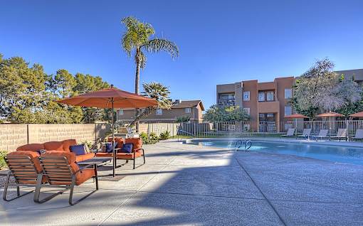 A pool area with chairs and umbrellas in front of a building.