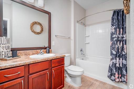 A bathroom with a toilet, sink, and a mirror at Overlook at Stone Oak Park Apartments, San Antonio