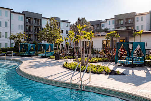 Pool deck with cabanas and palm tree landscaping at Avli At Crosstown Center Apartments, Florida