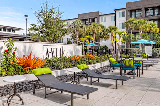 Property entrance sign with lounge chairs and landscaping at Avli At Crosstown Center Apartments, Florida