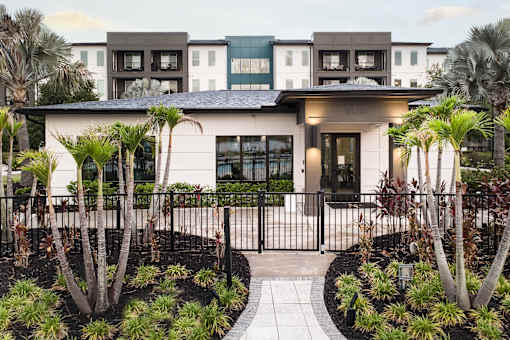 Clubhouse building with paver walkway and tropical landscaping at Avli At Crosstown Center Apartments, TAMPA, FL