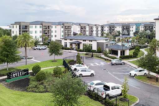 Gated property entrance with modern amenity buildings at Avli At Crosstown Center Apartments, Florida
